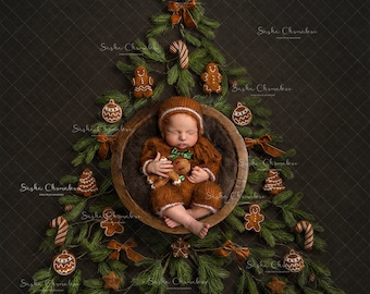 May include: A newborn baby wearing a brown knitted outfit is sleeping in a wooden bowl surrounded by a Christmas tree made of pine branches and decorated with gingerbread cookies, candy canes, and ornaments.