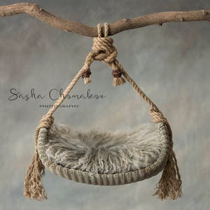May include: A brown, woven baby swing hanging from a branch. The swing is made of natural fibres and has a soft, fluffy lining. The swing is perfect for newborn photography props.