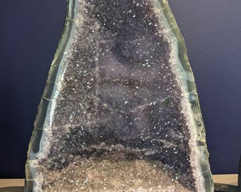 May include: A large amethyst geode with a dark purple interior and a crystalline structure. The geode is set on a black base and has a light-colored outer edge. A small tag with the numbers "15" and "260" is visible.