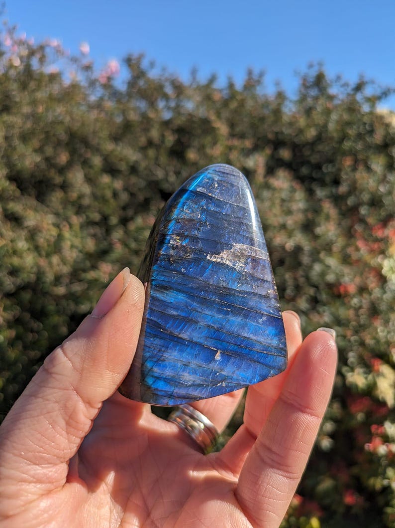 Puede incluir: Un cristal de labradorita azul y negro con forma de tri&aacute;ngulo. El cristal est&aacute; siendo sostenido en una mano.