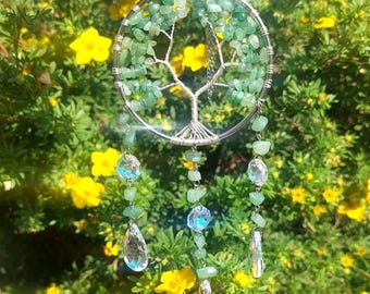 May include: A circular wall hanging featuring a wire-wrapped tree of life design made with small green aventurine stones. Three dangling strands extend from the bottom, each adorned with additional green stones and clear faceted crystal pendants.