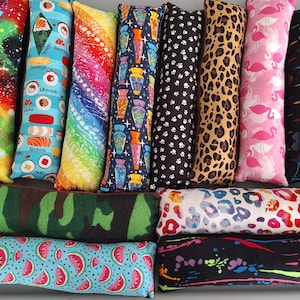 May include: A collection of twelve rectangular fabric cat kicker toys featuring various patterns including galaxy, sushi, rainbow, potion bottles, paw prints, leopard print, pink flamingos, heartbeats, camouflage, colorful animal spots, and watermelon slices.