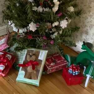 May include: A Christmas tree with white snowflake ornaments and red ribbon. Presents wrapped in red paper with red bows are scattered around the base of the tree. A green toy scooter is also present.