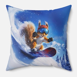 Op de afbeelding: Vierkant kussen met een cartoon eekhoorn die snowboardt van een besneeuwde berg. De eekhoorn draagt een rode muts, een bril en handschoenen. Het snowboard is rood en blauw, en de achtergrond toont een blauwe lucht en besneeuwde bergen.