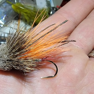 May include: A brown and orange fly fishing lure with a hook and feathers.