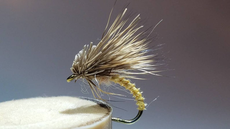 May include: A brown and tan fly fishing lure with a yellow body and a long, feathery tail.