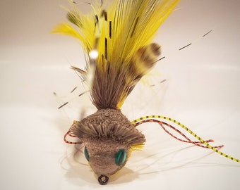 Può includere: Un'esca da pesca a mosca gialla e marrone con occhi verdi e una lunga coda di piume gialle.