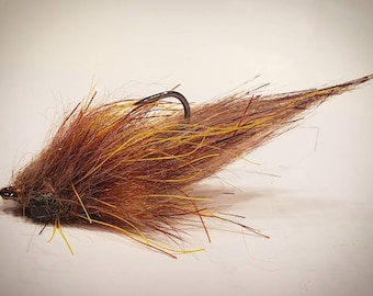 May include: A brown and yellow fly fishing lure with a long tail of feathers.