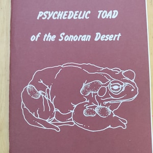May include: A book cover with a white illustration of a toad on a maroon background. The title is "Bufo alvarius: the PSYCHEDELIC TOAD of the Sonoran Desert" by Ken Nelson. The subtitle is "expanded and updated edition by Hamilton Morris".