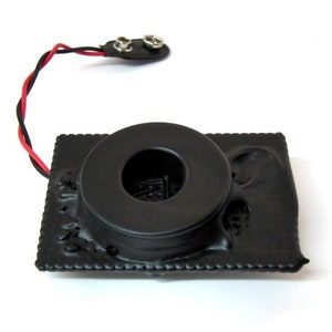 以下が含まれることがあります： 円形の巻線とワイヤーで接続されたバッテリーパックを備えた黒い電子部品