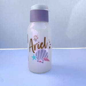 May include: White water bottle with a purple lid and a gold design that says "Ariel" with a seashell and starfish.
