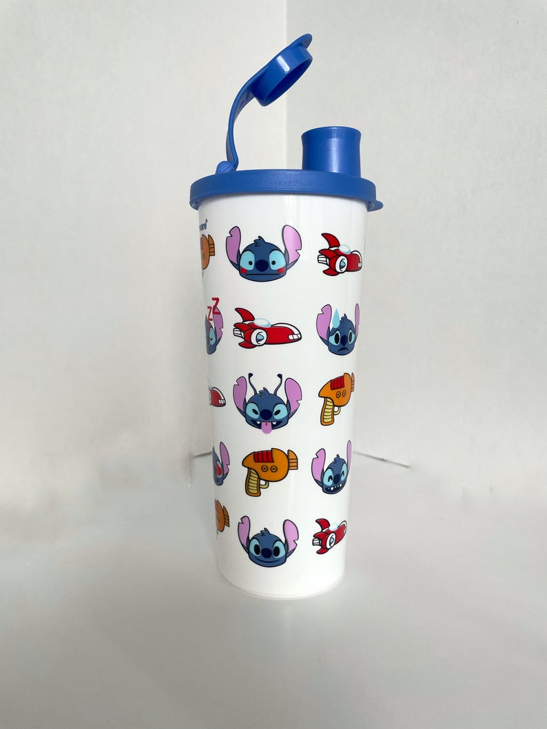 May include: A white reusable water bottle with a blue lid and a blue straw. The bottle has a repeating pattern of Stitch from Lilo & Stitch, spaceships, and laser guns.