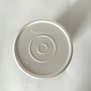 May include: White plastic lid for a container with the words "Tupperware", "Hecho en Mexico", "16oz", and "470ml" printed on it. The lid also has a recycling symbol and a symbol for microwave and dishwasher safe.