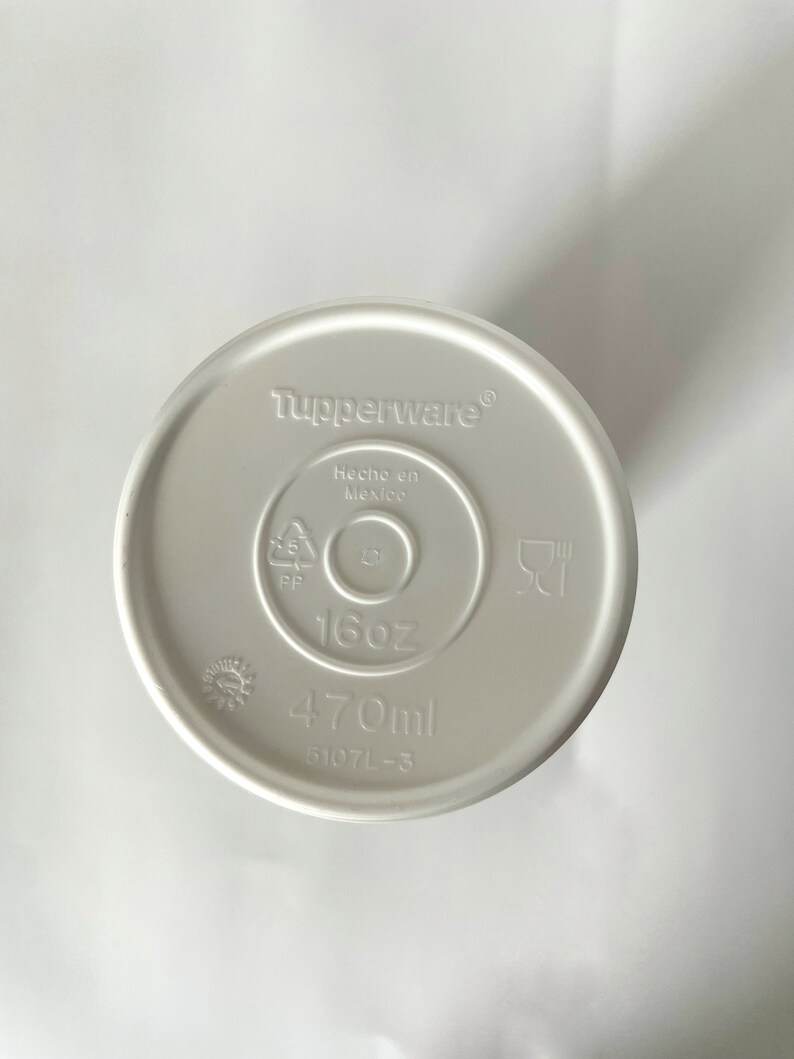May include: White plastic lid for a container with the words "Tupperware", "Hecho en Mexico", "16oz", and "470ml" printed on it. The lid also has a recycling symbol and a symbol for microwave and dishwasher safe.
