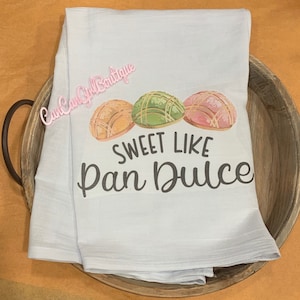 Puede incluir: Una toalla de cocina azul claro con un gr&aacute;fico de tres pasteles pan dulce y el texto "Sweet Like Pan Dulce".