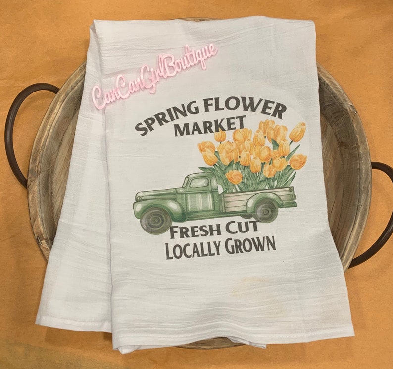 Puede incluir: Toalla de cocina blanca con un cami&oacute;n vintage verde que lleva un ramo de tulipanes amarillos. El texto dice "Spring Flower Market" y "Fresh Cut Locally Grown".