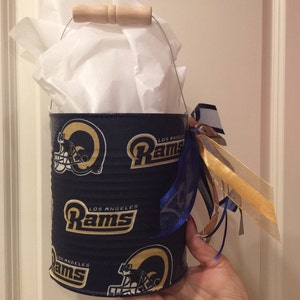 May include: A blue and gold Los Angeles Rams themed metal bucket with a wooden handle and blue and gold ribbon.