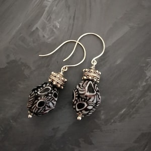 May include: A pair of silver dangle earrings featuring black and white patterned beads. The beads have a geometric design and are accented with silver.