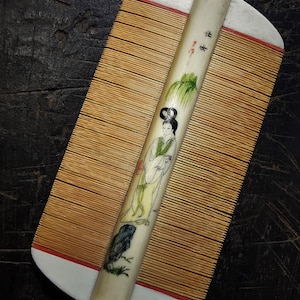 Puede incluir: Un peine blanco y marrón con un diseño pintado de una mujer con un vestido tradicional chino. El peine tiene un mango con los caracteres chinos "寿" y "字" escritos en él.