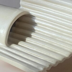 Pu&ograve; includere: Primo piano di un oggetto in ceramica color crema, a coste. L'oggetto ha un'apertura curva e cilindrica e una serie di creste parallele. Le creste creano una superficie strutturata e il design generale &egrave; semplice ed elegante.