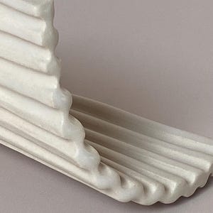 Pu&ograve; includere: Una modanatura architettonica decorativa color crema con un design a coste. La modanatura ha un bordo curvo ed &egrave; angolata, suggerendo che potrebbe essere utilizzata come mensola o finitura decorativa. Il pezzo &egrave; realizzato in un materiale solido, possibilmente simile alla pietra.