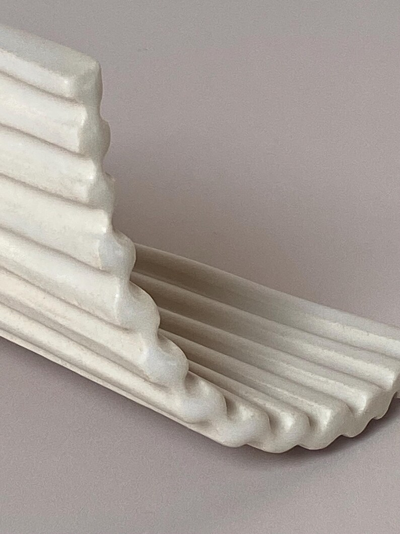 Pu&ograve; includere: Una modanatura architettonica decorativa color crema con un design a coste. La modanatura ha un bordo curvo ed &egrave; angolata, suggerendo che potrebbe essere utilizzata come mensola o finitura decorativa. Il pezzo &egrave; realizzato in un materiale solido, possibilmente simile alla pietra.