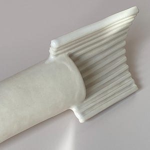 Pu&ograve; includere: Una scultura astratta bianca con una base cilindrica e una sommit&agrave; a forma di ventaglio. La parte superiore presenta una serie di creste orizzontali parallele. La scultura &egrave; realizzata in un materiale liscio e solido.