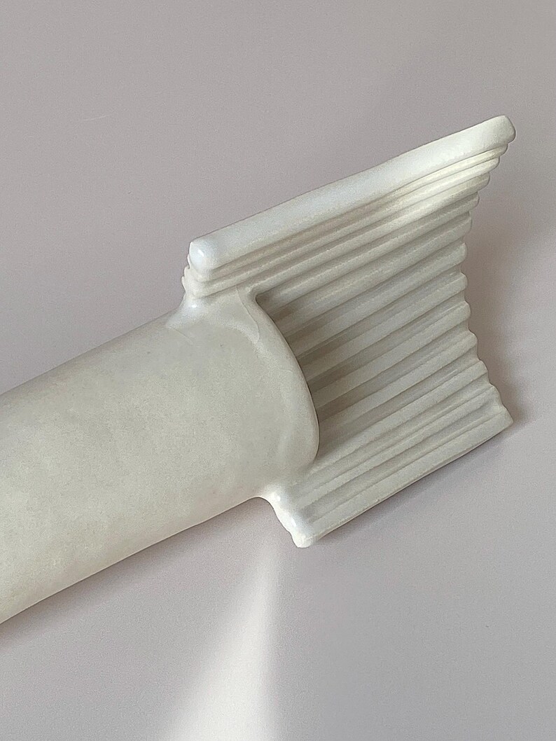 Pu&ograve; includere: Una scultura astratta bianca con una base cilindrica e una sommit&agrave; a forma di ventaglio. La parte superiore presenta una serie di creste orizzontali parallele. La scultura &egrave; realizzata in un materiale liscio e solido.