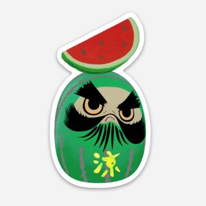 May include: A green daruma doll with a black and white face and a red watermelon slice on top. The doll has a black mustache and eyebrows and the word "水" in yellow on its chest.