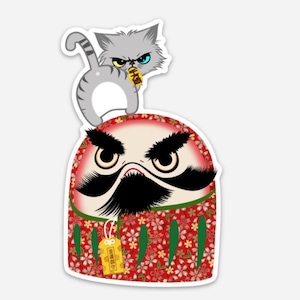 May include: A red and green daruma doll with a black mustache and eyebrows. A gray cat with blue eyes is perched on top of the doll's head.
