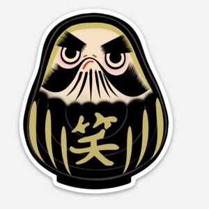 May include: A black and gold daruma doll with a scowling face and the Japanese character for "smile" written on its chest.