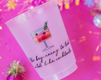 May include: A translucent frosted plastic cup featuring a graphic of a cocktail glass with a sprig of rosemary and two red berries. The text printed in black script reads, "It's beginning to look a lot like cocktails" below the illustration.
