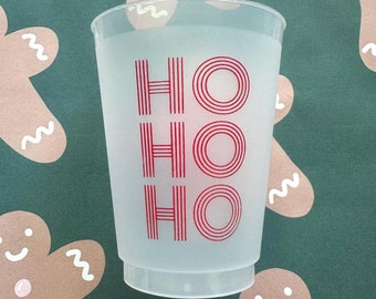 May include: A clear plastic cup with the word "HO HO HO" printed in red. The cup has a frosted appearance and is set against a green background with gingerbread man designs.