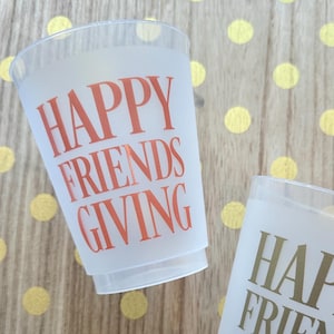 May include: Two clear plastic cups with the text "Happy Friends Giving" printed on them. One cup has orange text and the other has gold text.