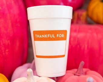 May include: A white foam cup with the text "THANKFUL FOR:" in orange, surrounded by a variety of colorful pumpkins in shades of pink, orange, and white. The pumpkins are of different sizes and shapes.
