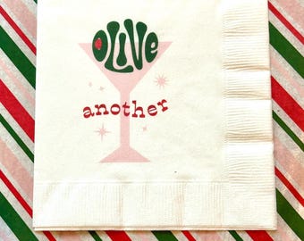 May include: White paper cocktail napkin with a pink martini glass and the words "olive" and "another" printed on it.