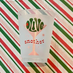 May include: A white plastic cup with a pink martini glass design and the words "olive" and "another" in red and green lettering.