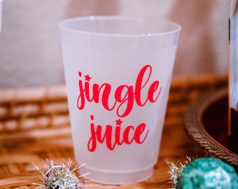 May include: A clear plastic cup with the words "jingle juice" in red script. The cup is on a woven surface, with Christmas ornaments and napkins nearby. Festive holiday drinkware.