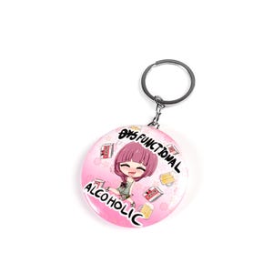 Puede incluir: Un llavero redondo rosa y blanco con una ilustración de dibujos animados de una niña y el texto "8/5 Funcional Alcohólico".