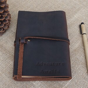 May include: A dark brown leather journal with a strap closure and the words "Adventure Awaits" embossed on the front.