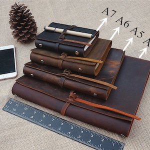 May include: Four brown leather journals of different sizes, labeled A4, A5, A6, and A7, stacked on top of each other. A ruler is in the bottom right corner of the image.