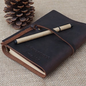May include: A brown leather journal with a pen and a brown leather strap. The journal has the words "Adventure Awaits" embossed on the front cover.