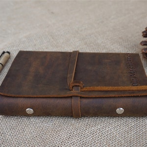 May include: A brown leather journal with a strap closure and the words "Our Adventures" embossed on the cover.