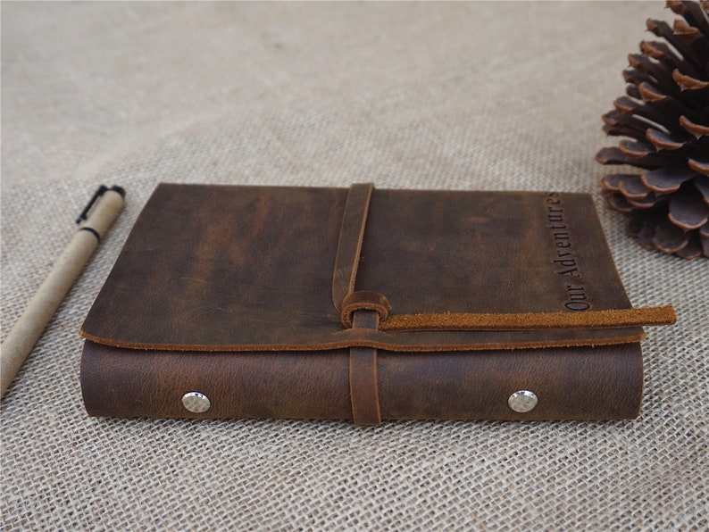 May include: A brown leather journal with a strap closure and the words "Our Adventures" embossed on the cover.