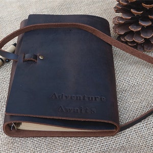 May include: A brown leather journal with a strap closure and the words "Adventure Awaits" embossed on the front.
