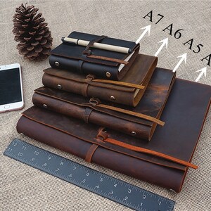 May include: Four brown leather journals of different sizes, labelled A4, A5, A6, and A7, stacked on top of each other. A ruler is in the foreground.