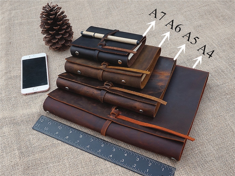 May include: Four brown leather journals of different sizes, labelled A4, A5, A6, and A7, stacked on top of each other. A ruler is in the foreground.