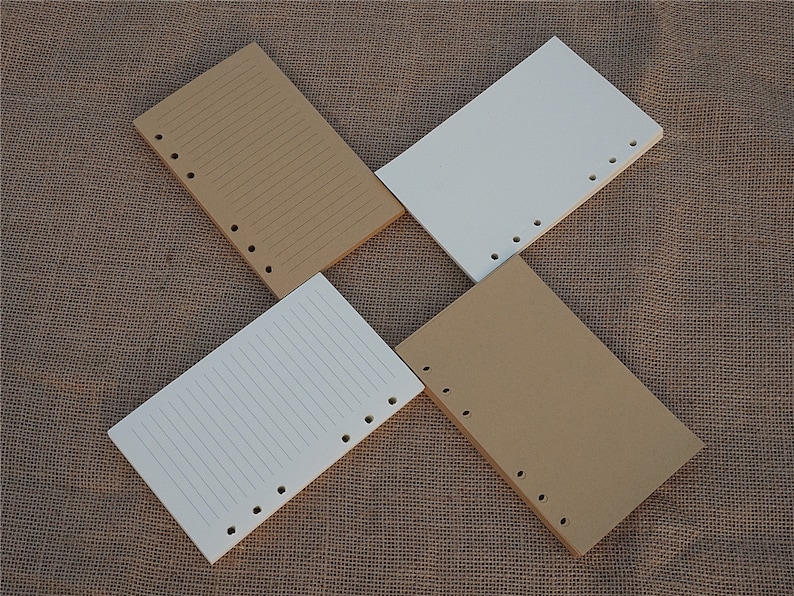 May include: Four sheets of paper with holes punched along the side. Two sheets are brown and two sheets are white. The sheets are lined and are lying on a brown burlap surface.