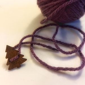 Könnte beinhalten: Ein Knäuel tiefvioletter Wolle mit passendem Kordel und einem kleinen Weihnachtsbaumschmuck aus Holz. Die Wolle und die Kordel haben einen ähnlichen Lilaton. Der Holzschmuck ist dunkelbraun.