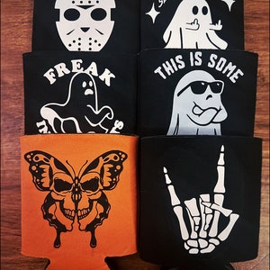 May include: Six black and orange can coolers with various Halloween-themed designs. The designs include a ghost with sunglasses, a ghost giving the finger, a skull butterfly, a skeleton hand, a ghost with a creepy smile, and a hockey mask.